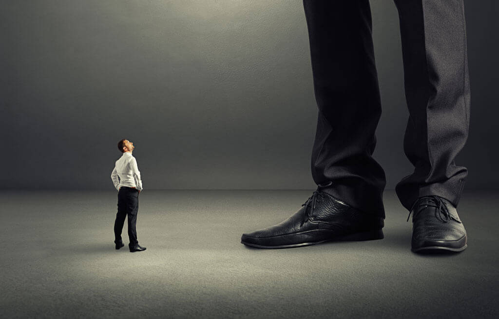 man standing at feet of a large pair of legs depicting how hotels feel smaller that otas