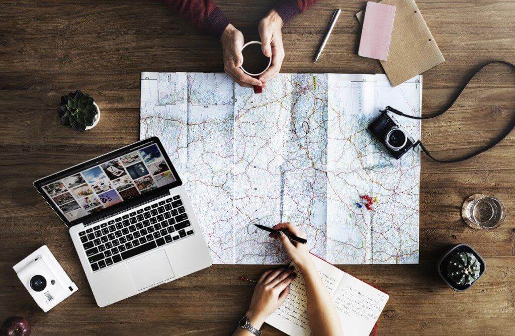 two people looking at a map with a laptop and camera near by as they plot their travel