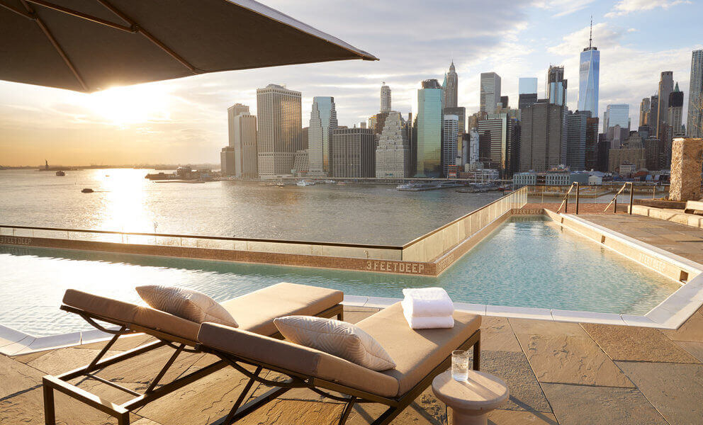 hotel website image showing sunloungers by a pool looking over new york skyline a unique guest experience