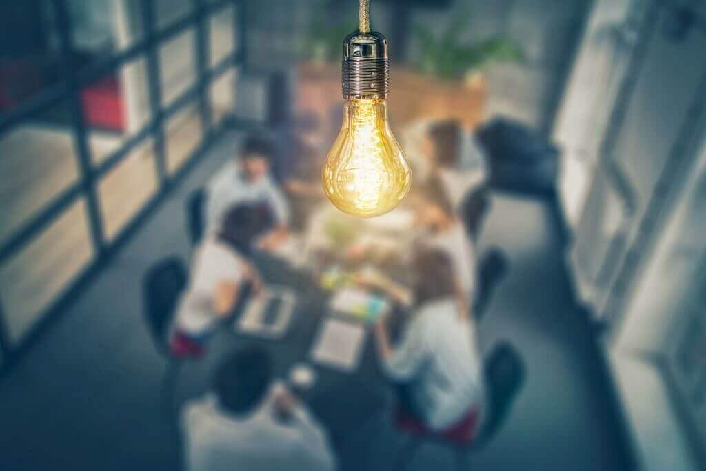 lightbulb if front of people from different hotel departments sitting at a desk working together to come up with ideas to drive revenue