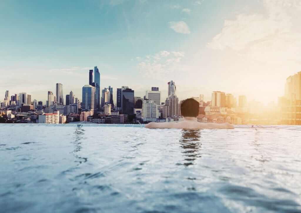 man in a pool looking at bangkok skyline on travel trip