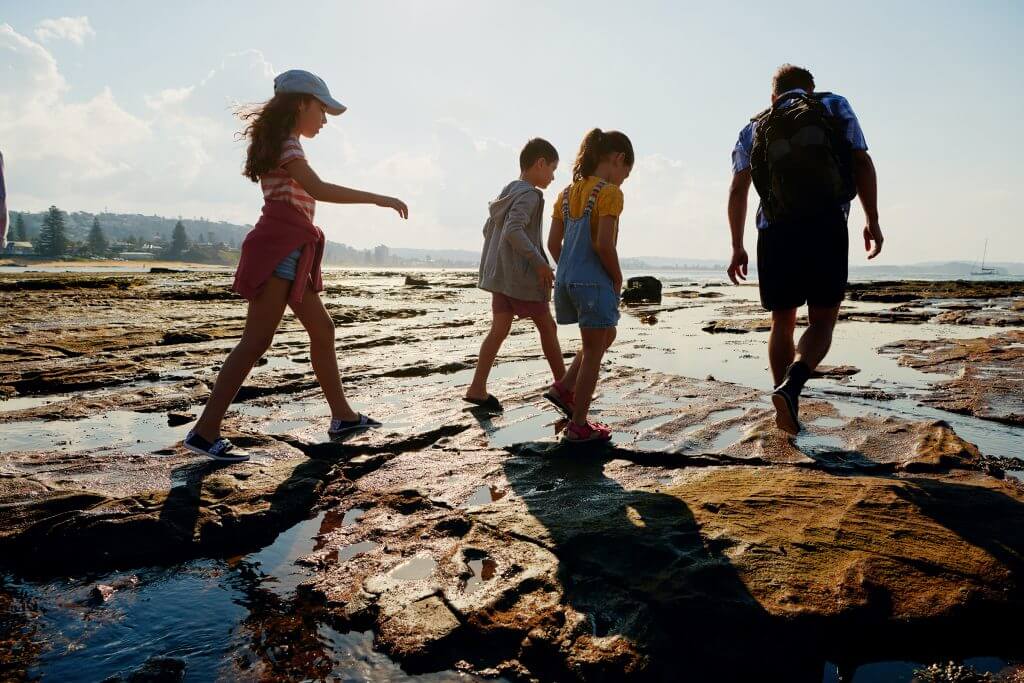 family walking on wet stone near shoreline by hotel