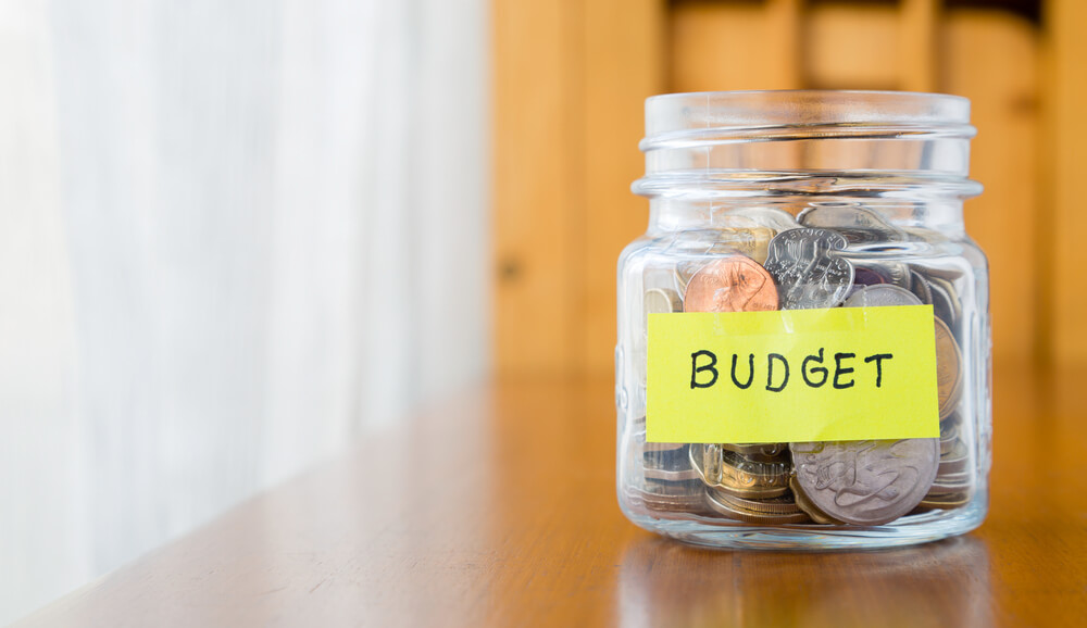 glass jar with money inside and the word budget written on a label on the front as we enter important period for budgeting