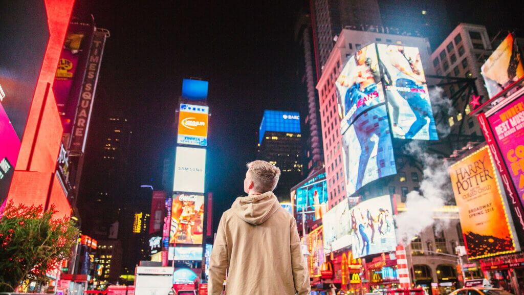 young lad looking up in amazement at the bright lights in New York illustrating importance for hotels to position their property for shoulder season bookings through destination marketing strategies