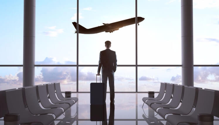 business traveler in airport lounge looking at a plane taking off