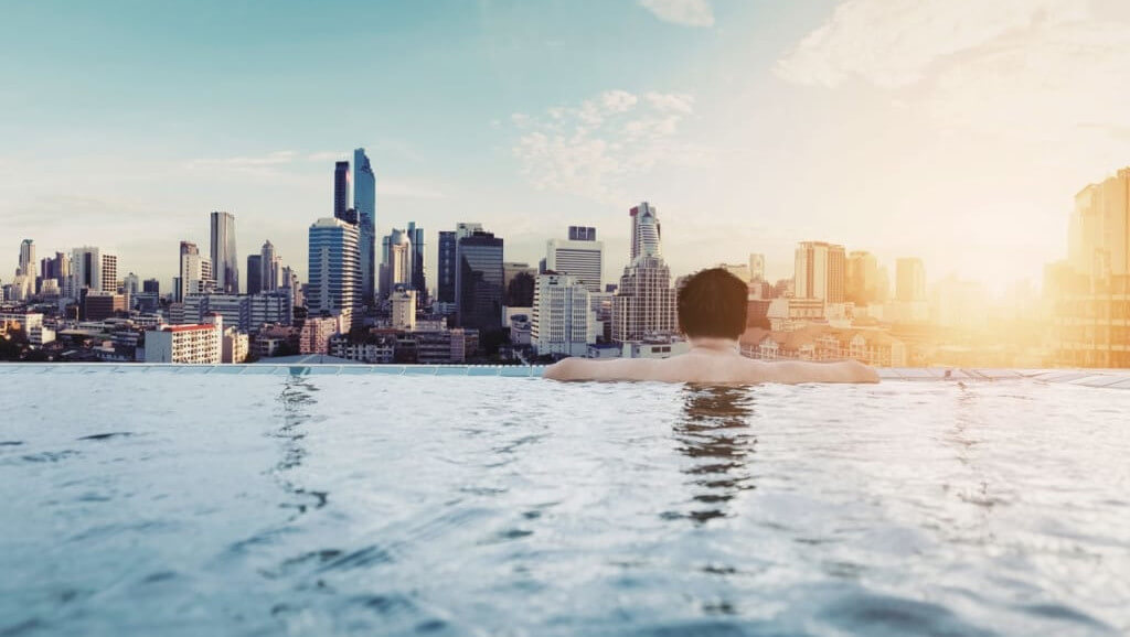 man in hotel pool looking out of city skyline reflecting positive impact of hotels identifying guest expectations to deliver strong feedback, reviews and reputation