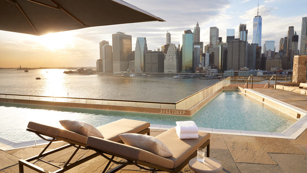 2 sun loungers beside a hotel pool overlooking new york skyline