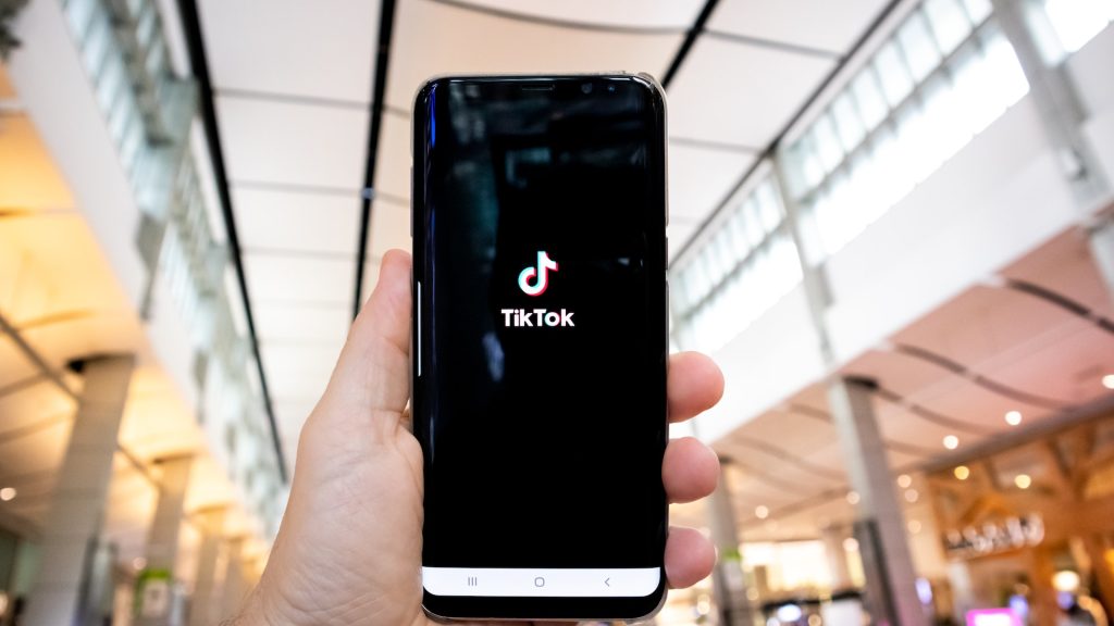 person holding a mobile phone with tiktok logo in a hotel lobby reflecting importance in driving direct revenue