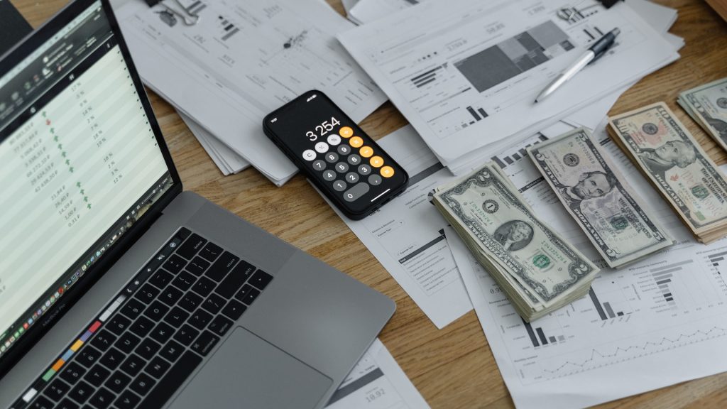 laptop calculator graphs and dollars reflecting the importance of total revenue management in hotel profitability strategy