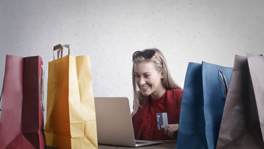 person looking at a laptop with shopping bags and a credit card reflecting the importance for hotels to explore merchandise options to drive additional hotel revenue
